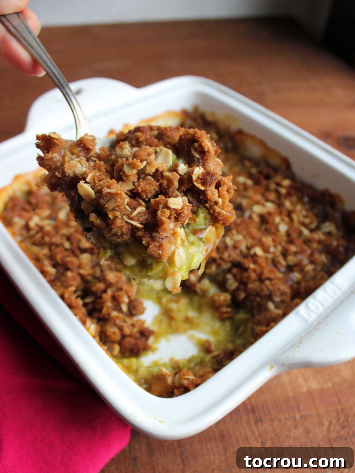 Vintage serving spoon scooping out a helping of old fashioned rhubarb crisp showing the thickened rhubarb filling and browned oatmeal crisp topping. 