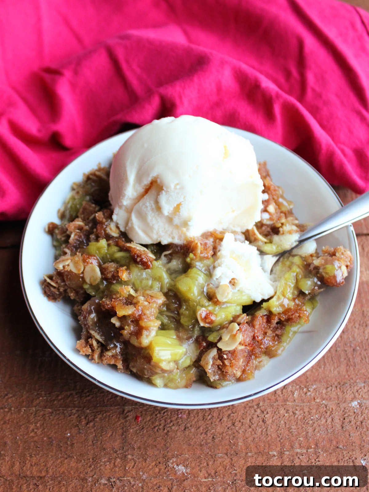 Bite of rhubarb crisp and vanilla ice cream on spoon, ready to eat. 