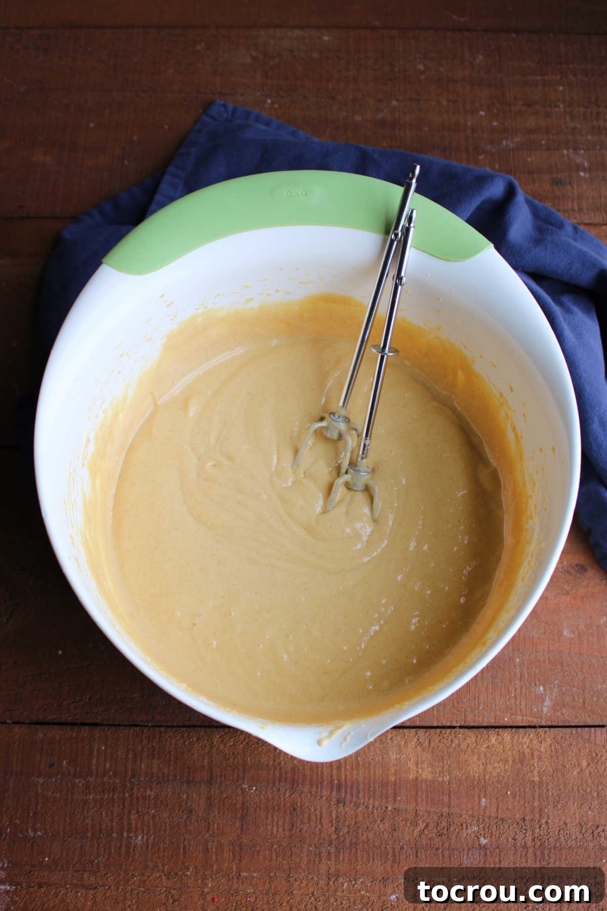 Mixing Peanut Butter Cake Batter for Poke Cake A large mixing bowl filled with creamy peanut butter cake batter, with electric mixer beaters resting inside, ready for the next step of baking.