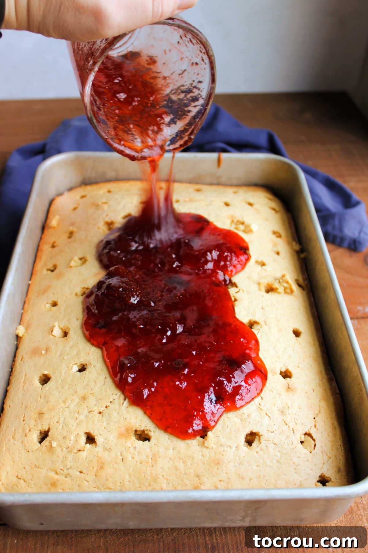 Infusing Jelly into Warm Poke Cake Warm strawberry jelly being generously poured over a freshly baked 9x13 inch peanut butter cake, which has been pre-poked with numerous holes to absorb the fruity sweetness.