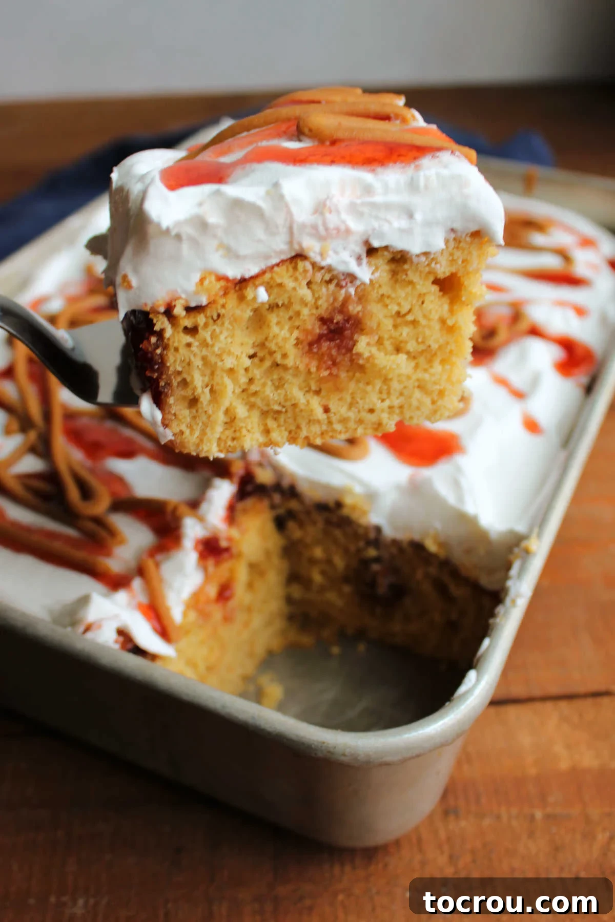 Serving a Slice of Peanut Butter and Jelly Poke Cake A spatula carefully lifts a perfect piece of peanut butter and jelly poke cake from a 9x13-inch baking pan, revealing the soft texture and the remaining cake ready for serving.