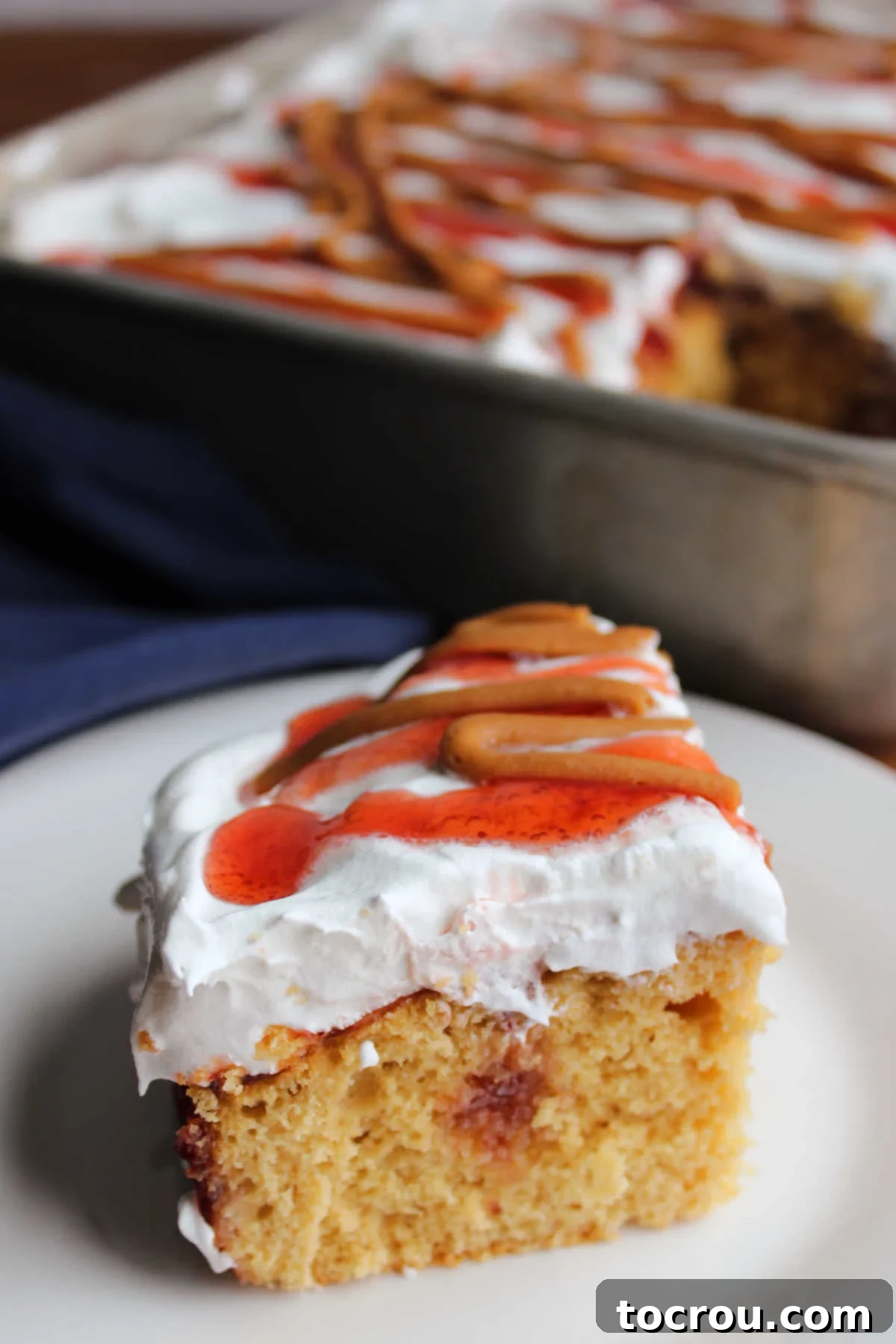 Detailed View of PB&J Poke Cake with Jelly Tunnels A close-up of a delightful slice of peanut butter and jelly poke cake, showcasing a clear tunnel of luscious strawberry jelly embedded within the moist peanut butter cake, perfectly ready to be savored.