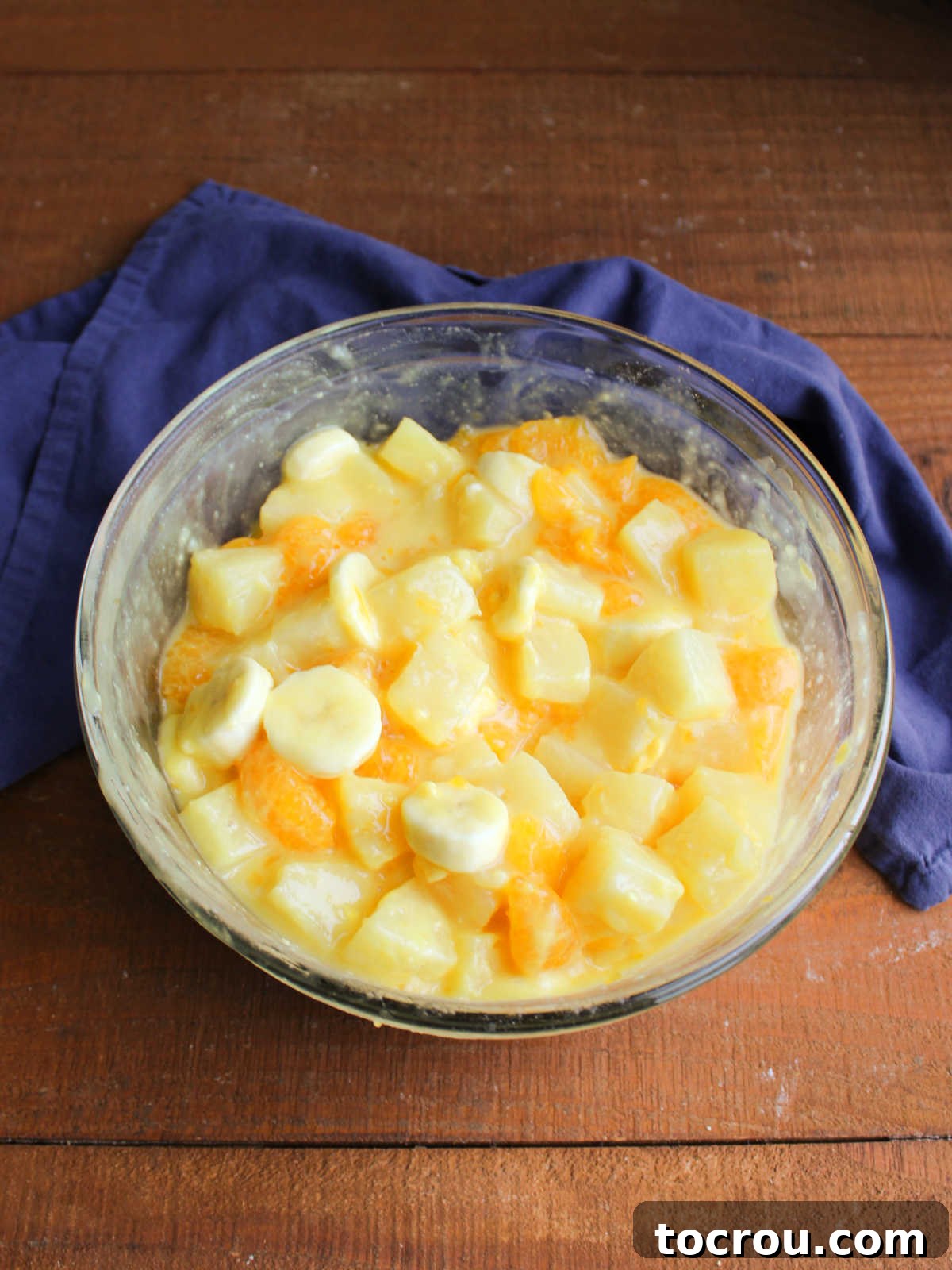 Mixing bowl of fruit after instant pudding powder has been stirred in to make a creamy dressing.