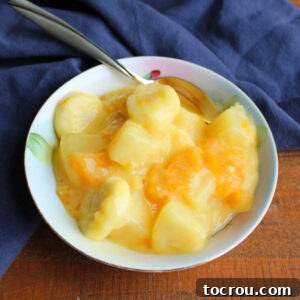 Small bowl filled with fruit salad made from bananas, mandarin oranges, and pineapple in creamy vanilla pudding dressing.