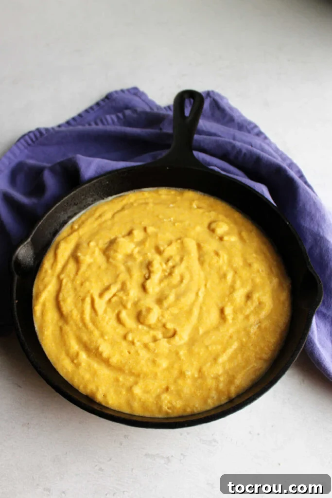 Cornbread batter perfectly poured into a seasoned cast iron skillet, ready for baking. 9 inch cast iron skillet filled with cornbread batter, ready to bake.