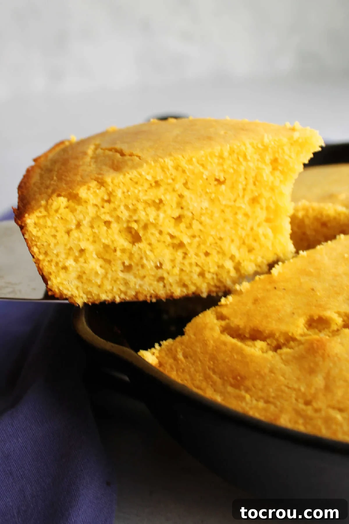 A perfect slice of soft, yellow cornbread being lifted from a cast iron skillet. Lifting slice of soft yellow cornbread out of cast iron skillet.