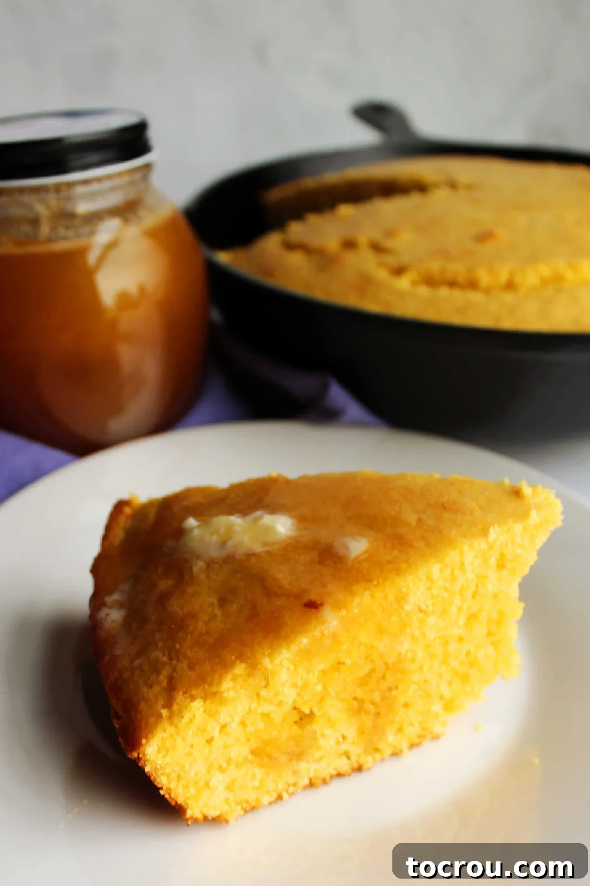 A delicious slice of skillet cornbread, generously topped with melting butter and golden honey. Slice of cornbread with honey and butter on top.