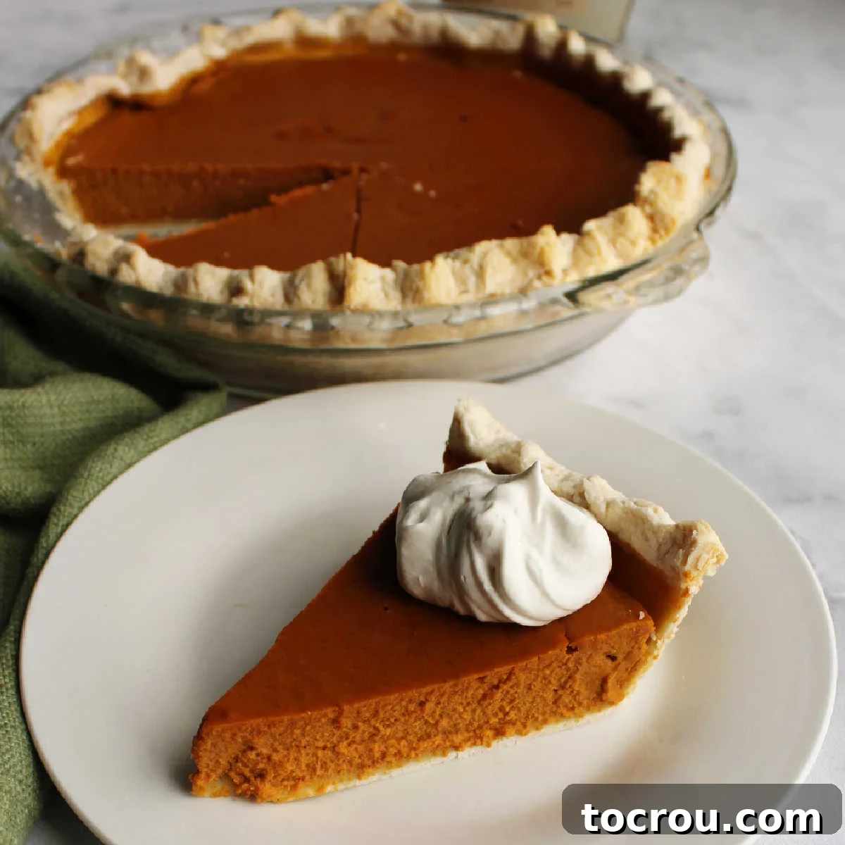 A perfectly sliced maple pumpkin pie, generously topped with maple whipped cream, stands in front of the remaining pie, inviting a taste.