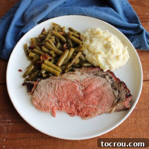 Dinner plate with a piece of medium rare prime rib, smothered green beans, and mashed potatoes.