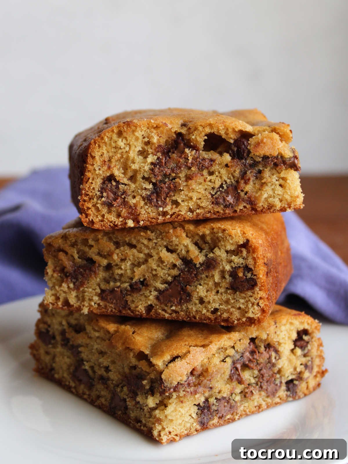 Three golden-brown sourdough chocolate chip cookie bars stacked neatly, showcasing their appealing texture and ready to be enjoyed.
