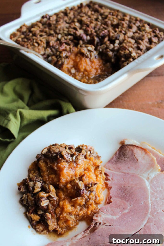 Maple crunch sweet potato casserole served with ham on a dinner plate.
