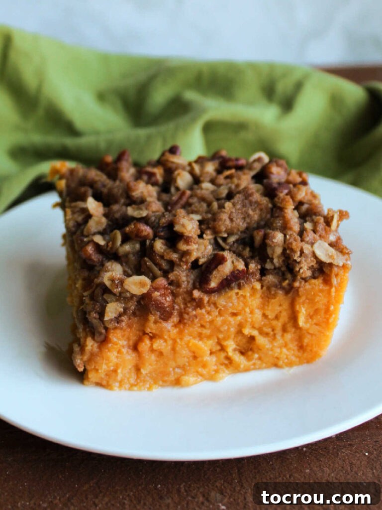 Piece of smooth maple sweet potato casserole topped with crunchy pecan, oatmeal and brown sugar topping on small white plate.
