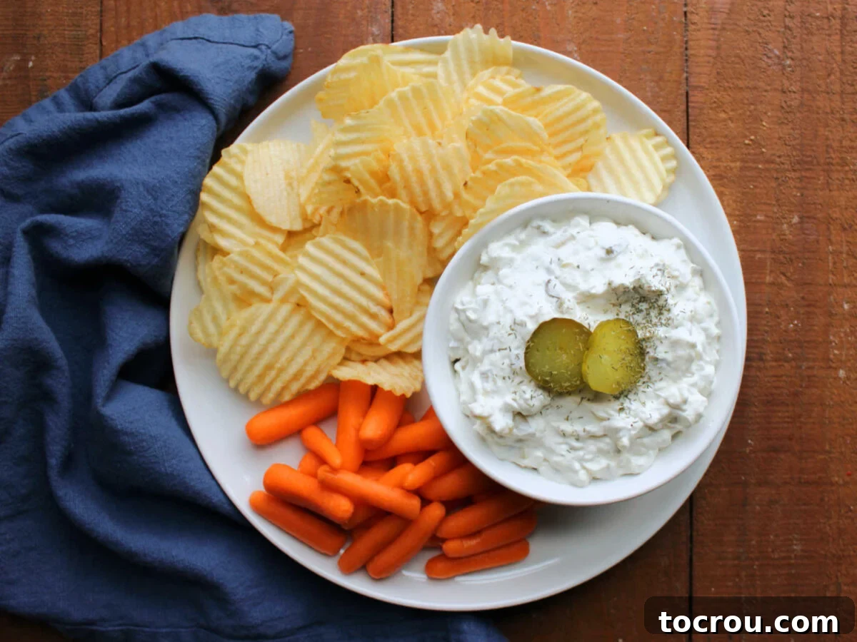 Creamy Dill Delight 2 Looking down on a plate with a bowl of homemade dill pickle dip served with ruffled potato chips and baby carrots.