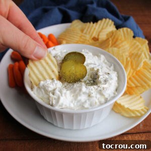 Hand dipping a chip into a bowl of cream dill pickle dip.