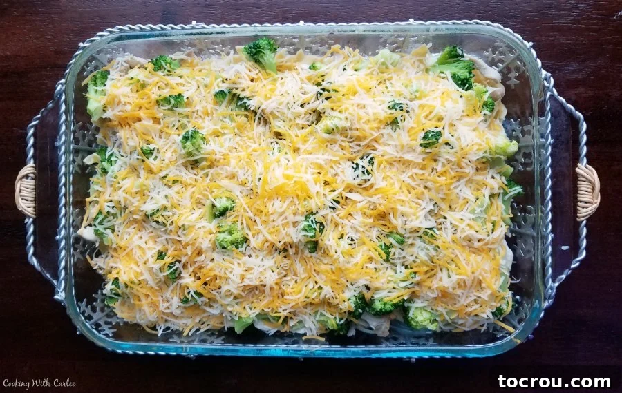 A 9x13 baking dish filled with a delicious mixture of pasta, chicken, and broccoli, topped with shredded cheese, ready to be baked into a comforting casserole.