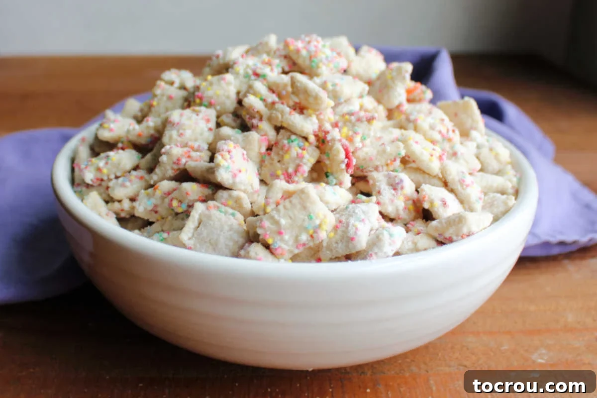 Serving bowl piled high with birthday cake puppy chow coated in white chocolate, sprinkles, and funfetti cake mix. 