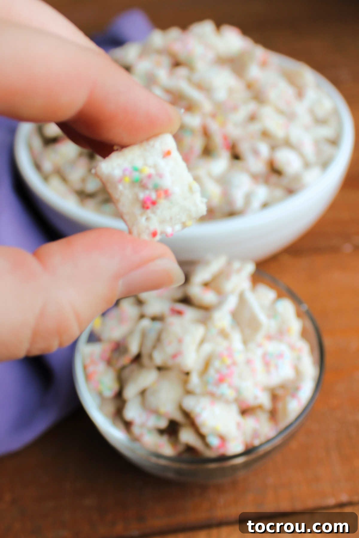 Hand holding piece of funfetti puppy chow with white chocolate and sprinkle coating. 