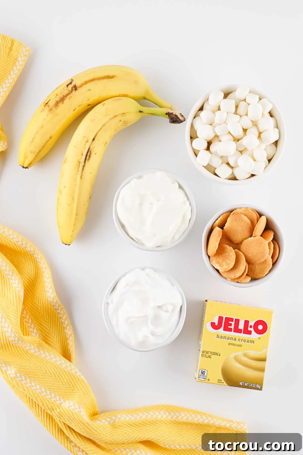 Ingredients including fresh bananas, mini marshmallows, instant pudding mix, cool whip, and sour cream ready to be made into banana pudding fluff salad. 