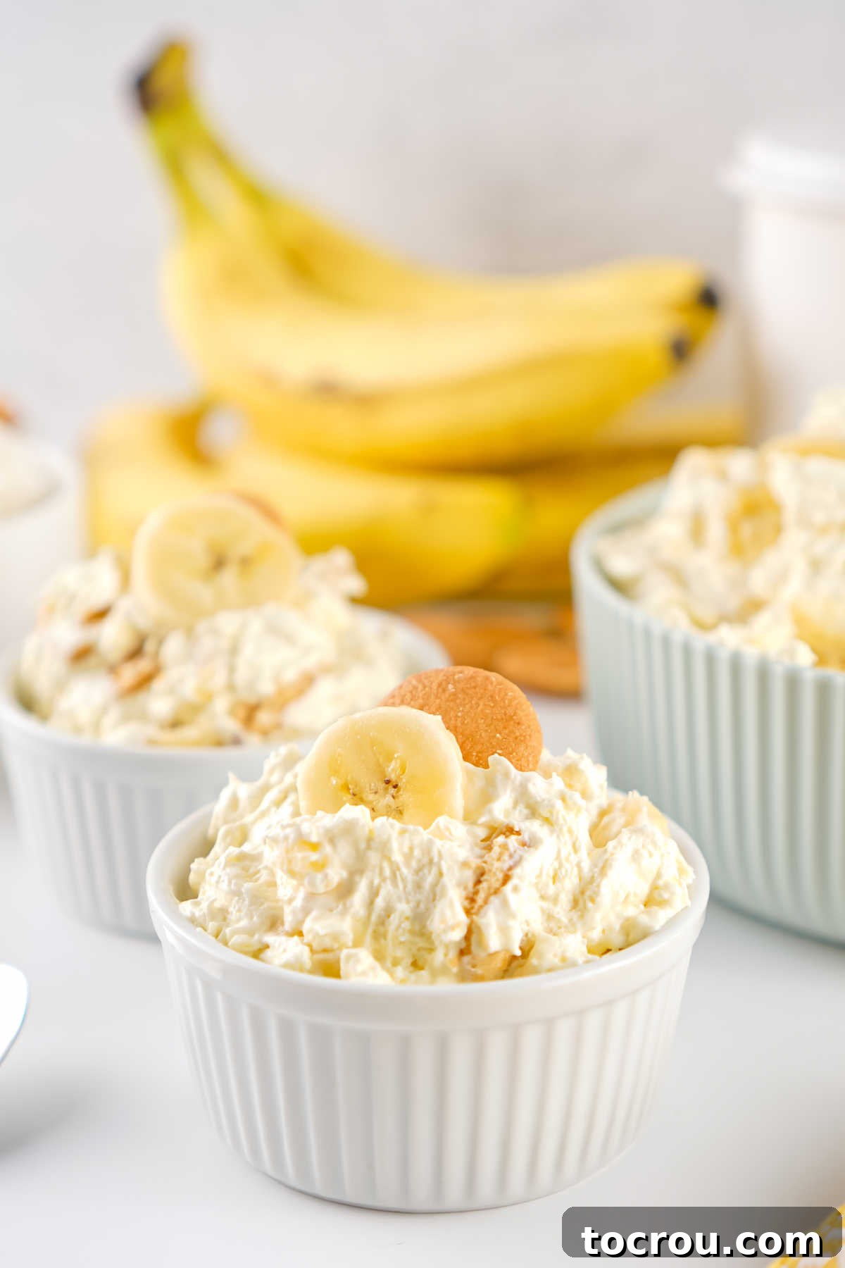 Two ramekins with helpings of banana pudding fluff salad topped with extra banana slices and a nilla wafer, ready to eat. 