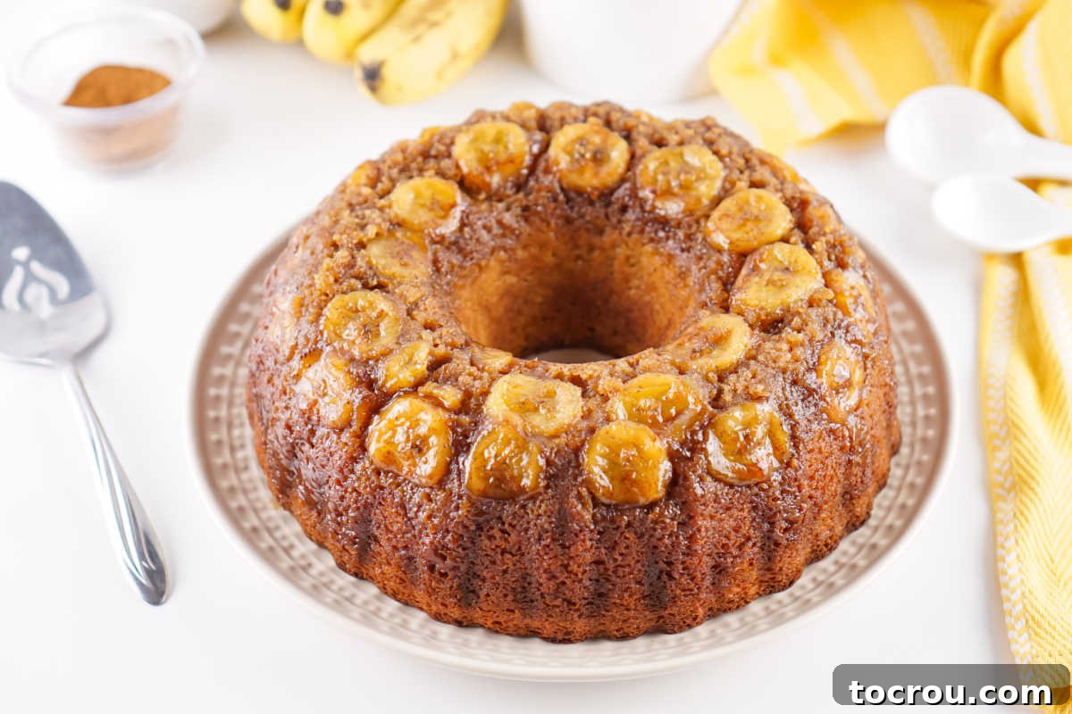 Whole banana upside down cake on cake plate with server nearby, ready to be sliced and served.
