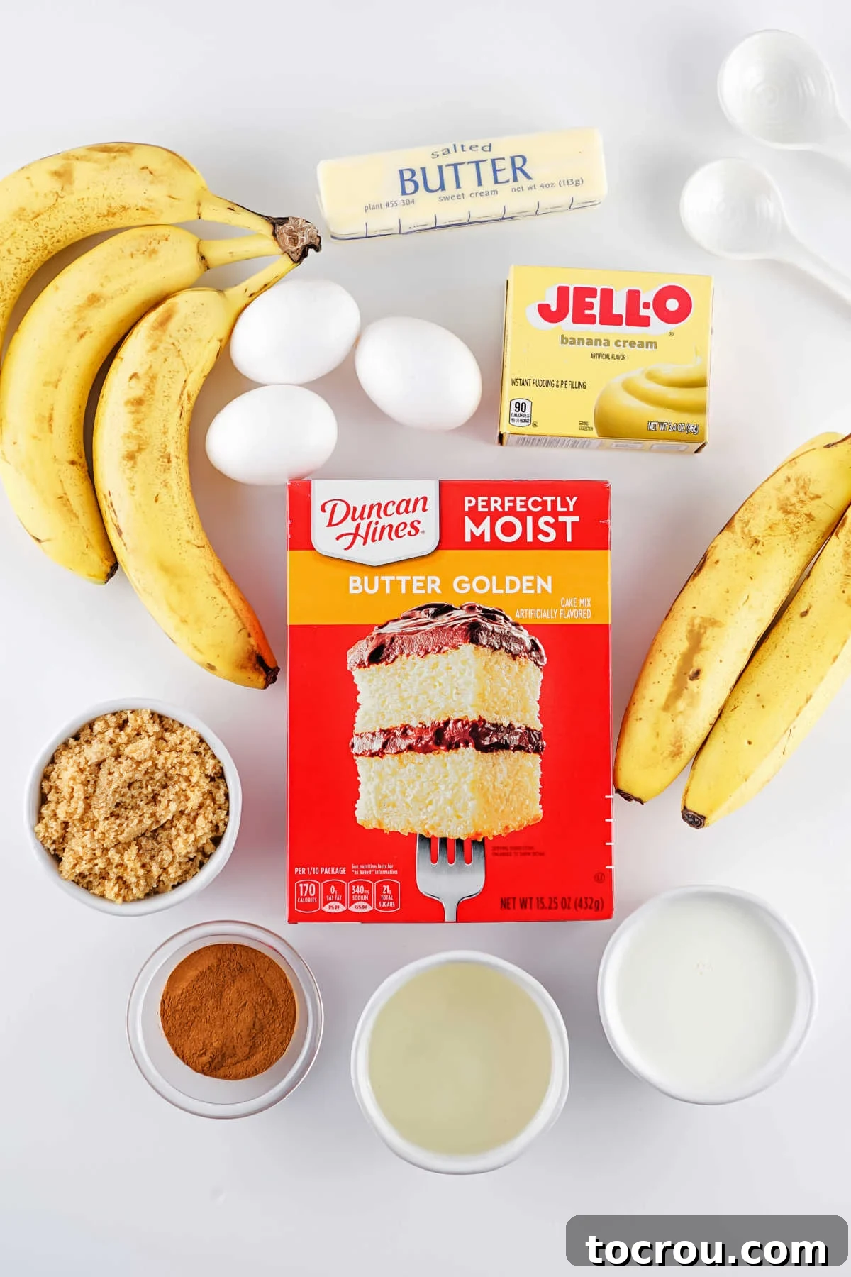 Ingredients including butter cake mix, instant pudding mix, bananas, oil, butter, brown sugar, eggs, and cinnamon ready to be made into a banana upside down bundt cake.