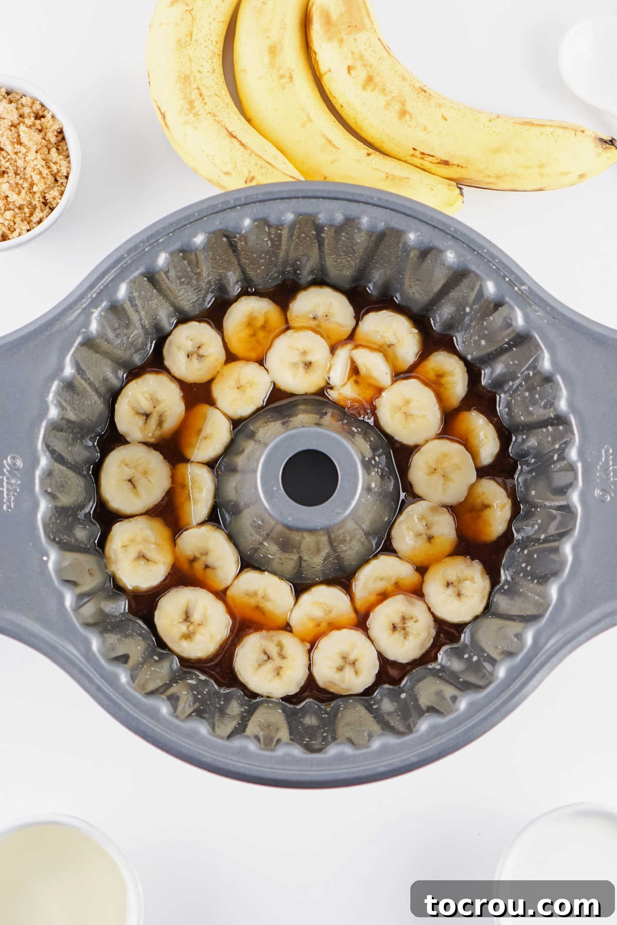 Bundt cake pan with melted butter and brown sugar mixture and sliced bananas in the bottom, ready for batter.
