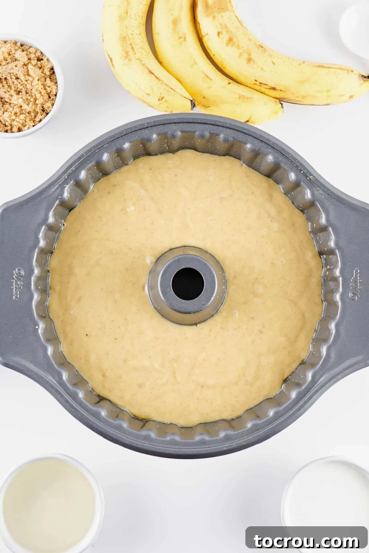 Banana cake batter in bundt cake pan over top of the banana slices and brown sugar, ready to go in the oven.