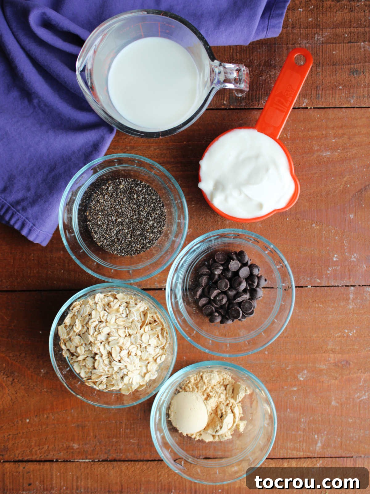 Ingredients for peanut butter overnight oats including milk, yogurt, chia seeds, oats, peanut butter powder, and chocolate chips.