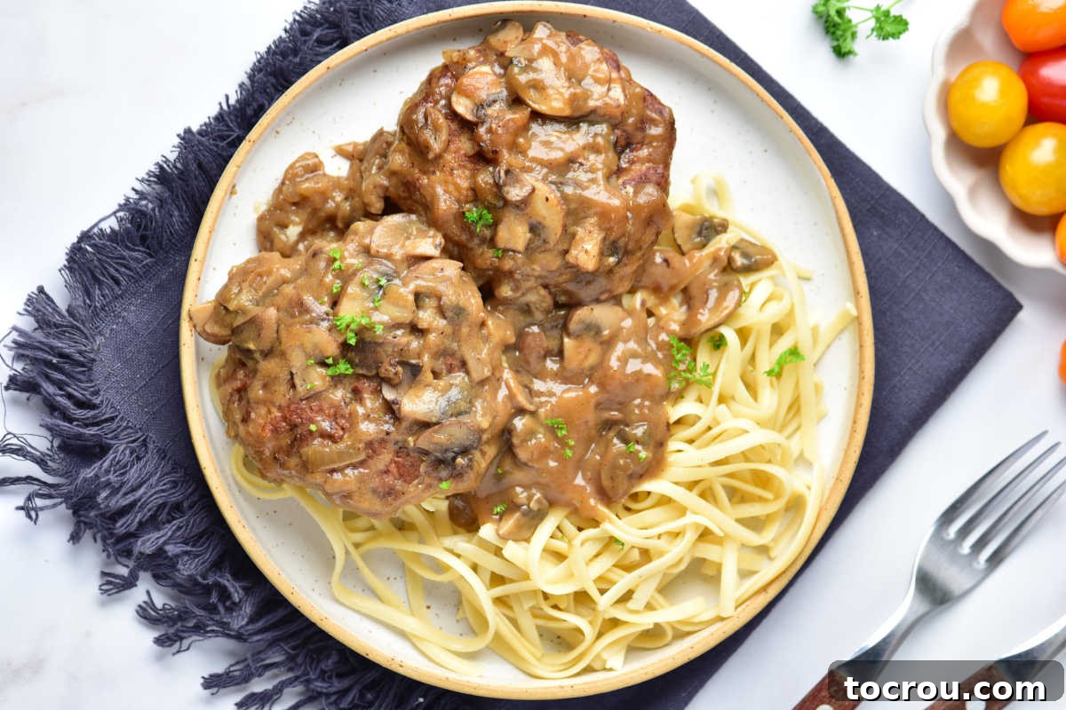 Turkey Salisbury Steaks with Mushroom Gravy Turkey salisbury steaks in rich mushroom gravy served over egg noodles with fork nearby.