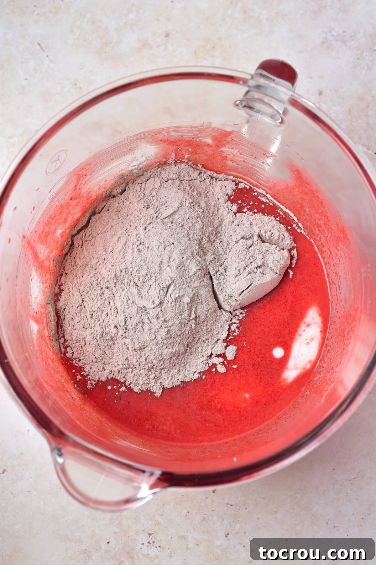 Blending Wet and Dry Ingredients for Red Velvet Cake Batter Mixing dry ingredients into wet ingredients in large glass mixing bowl.