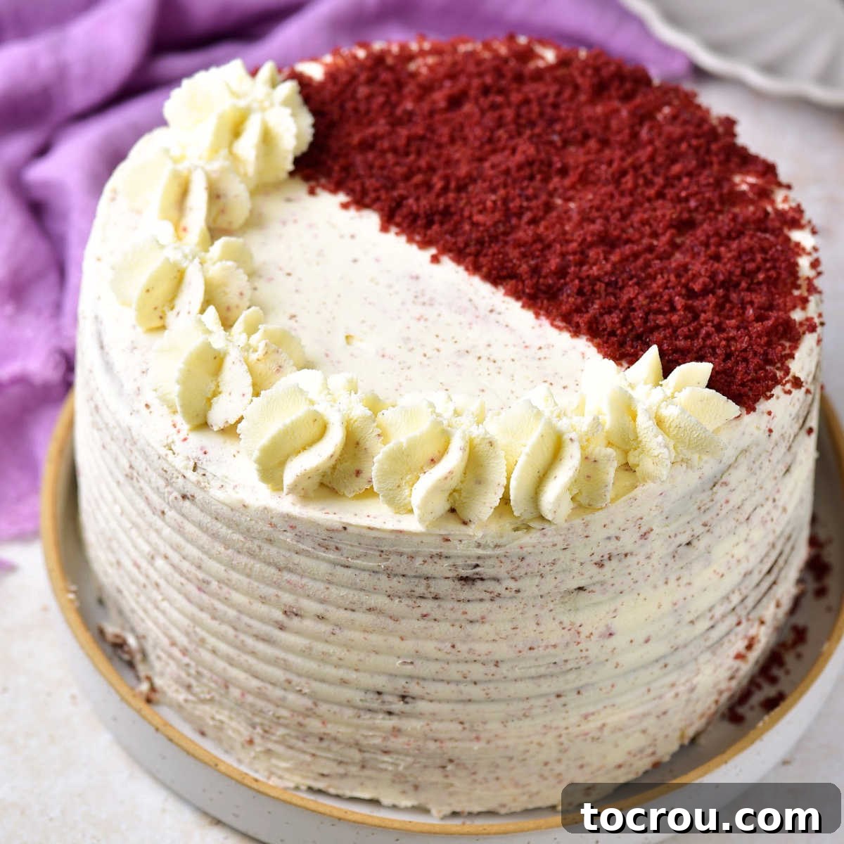 Elegant Red Velvet Layer Cake with Mascarpone Frosting Red velvet layer cake with mascarpone frosting surrounding it and piped mascarpone frosting and red velvet cake crumbs decorating the top.