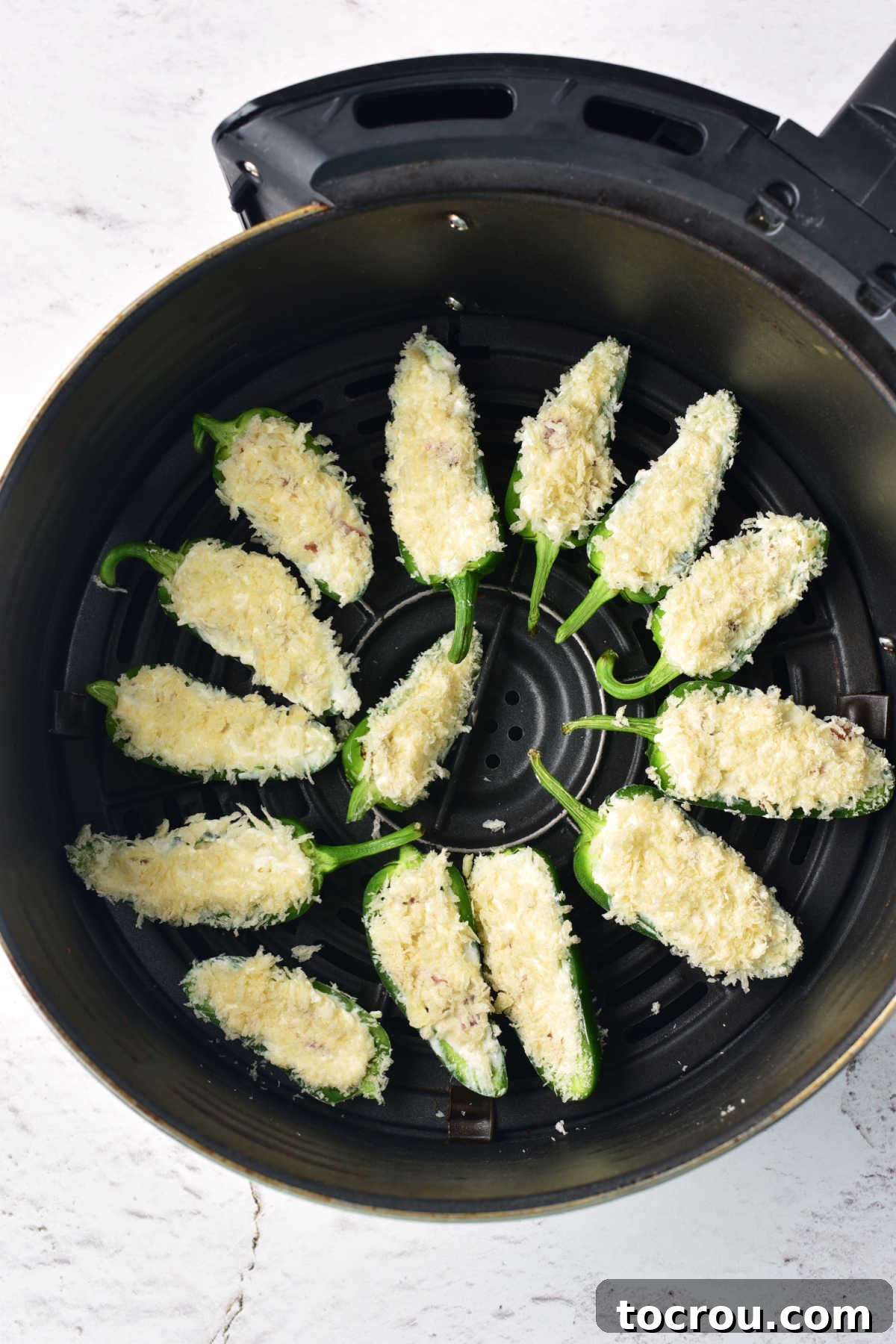 Jalapeno Poppers Ready for Air Frying Stuffed jalapeno peppers with panko bread crumbs pressed into the cream cheese mixture in an air fryer basket ready to cook.