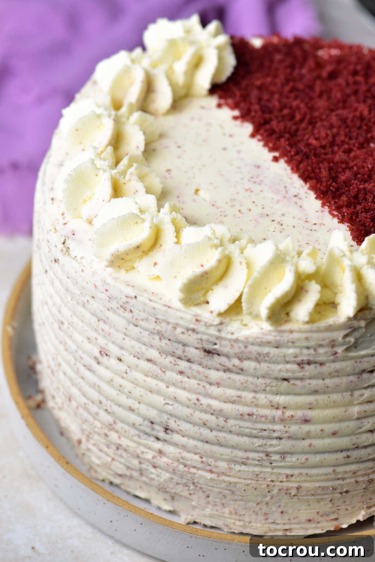 Velvet Mascarpone Frosting 6 Close up of the side of a red velvet cake with a thin layer of mascarpone frosting spread over it and some piped mascarpone frosting on top.