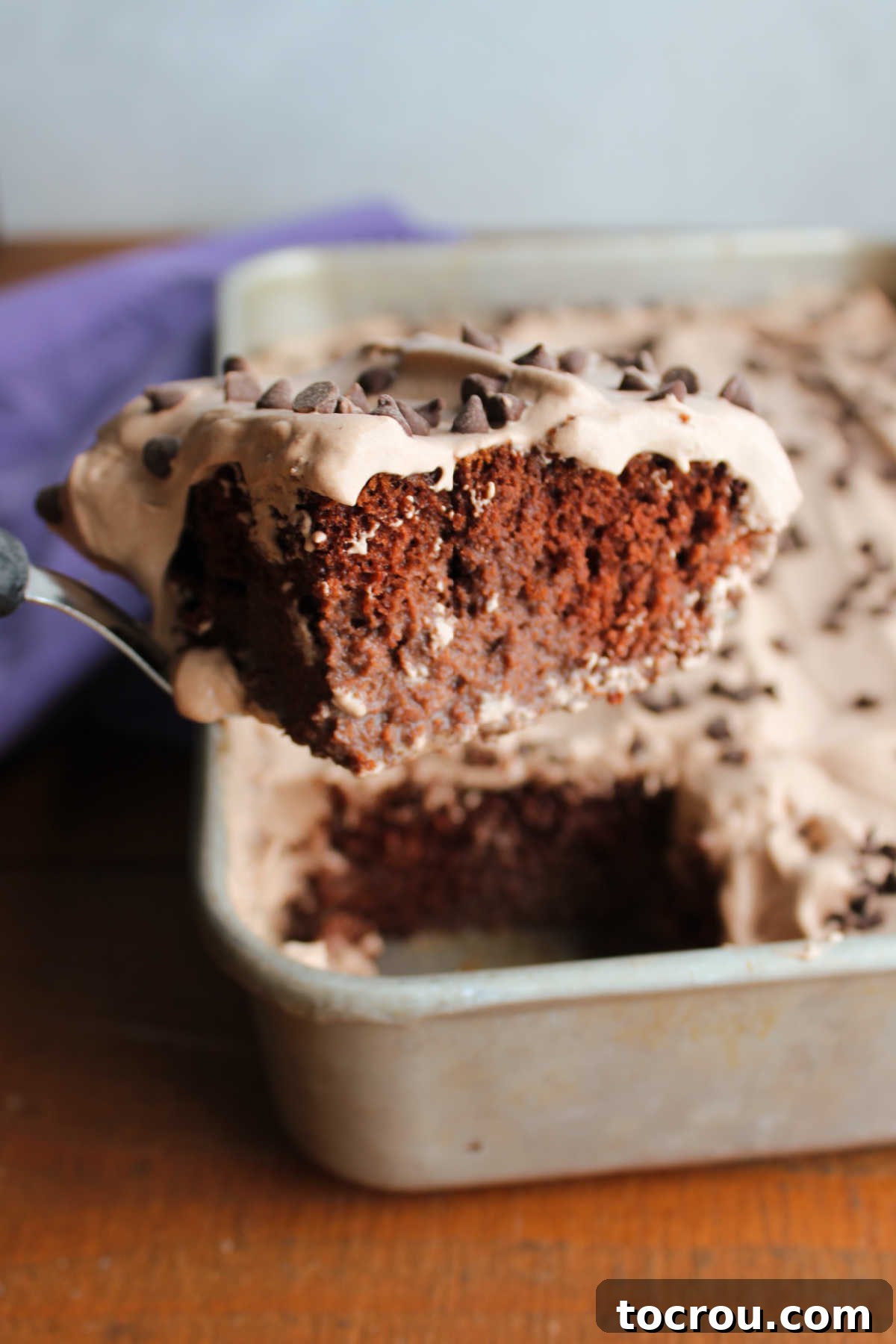 Triple-Milk Chocolate Dream 5 Spatula lifting slice of chocolate tres leches cake out of pan showing milk soaked cake texture and fluffy chocolate whipped cream on top.