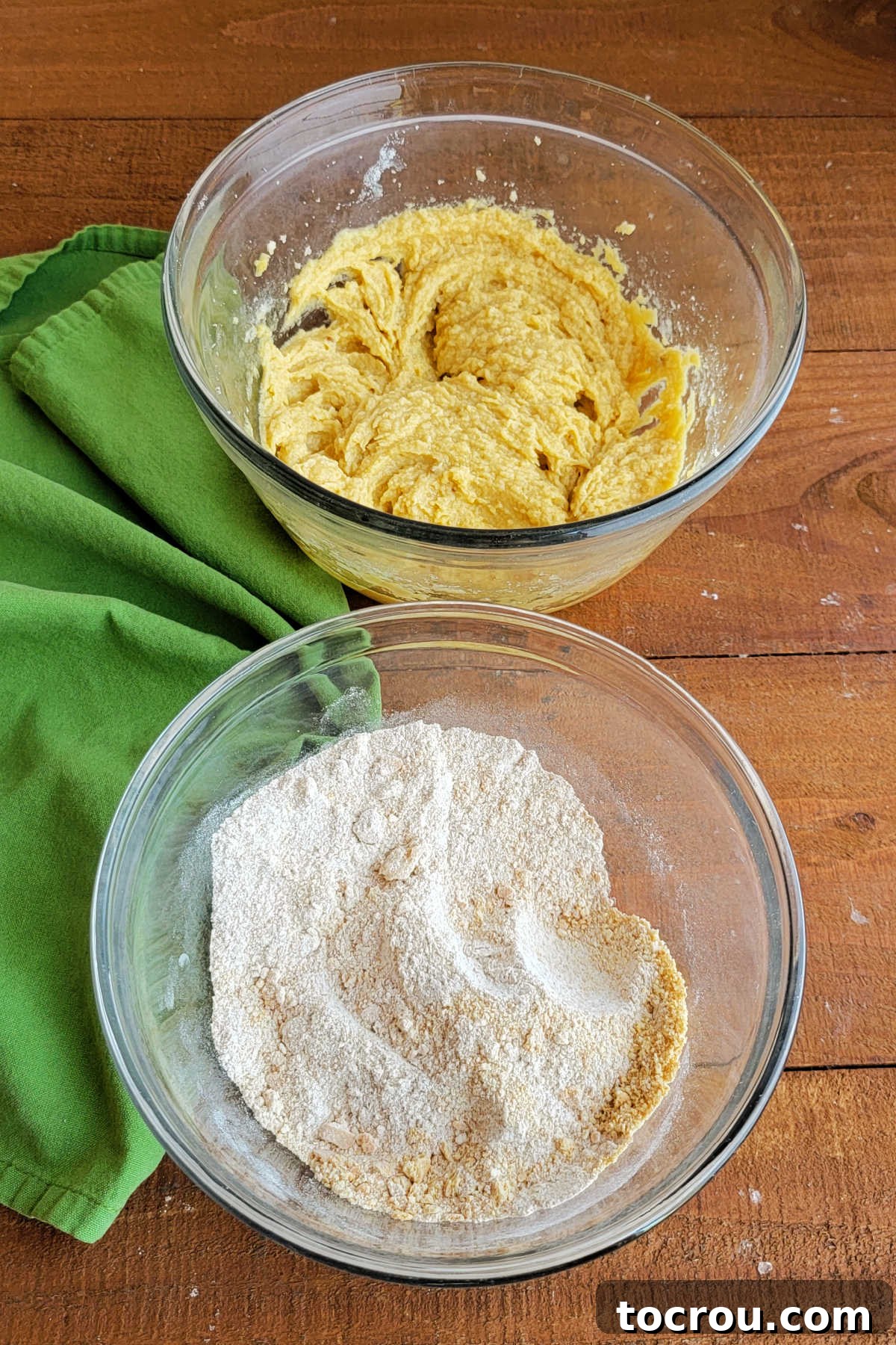 Mixing bowl of butter, sugar and egg mixture next to mixing bowl with dry ingredients ready to be combined into graham cookie dough. 