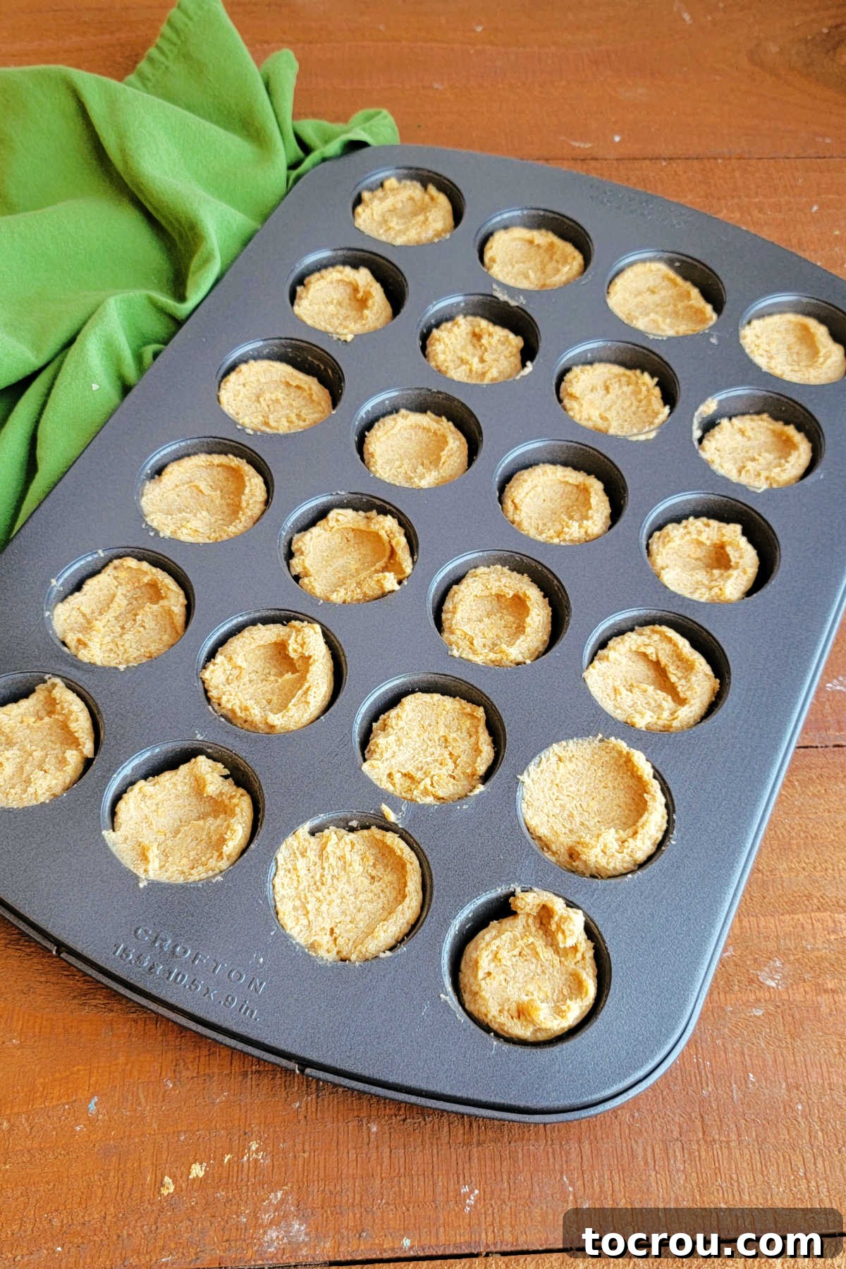 Thick graham cracker cookie dough in greased mini muffin tray, ready to bake. 