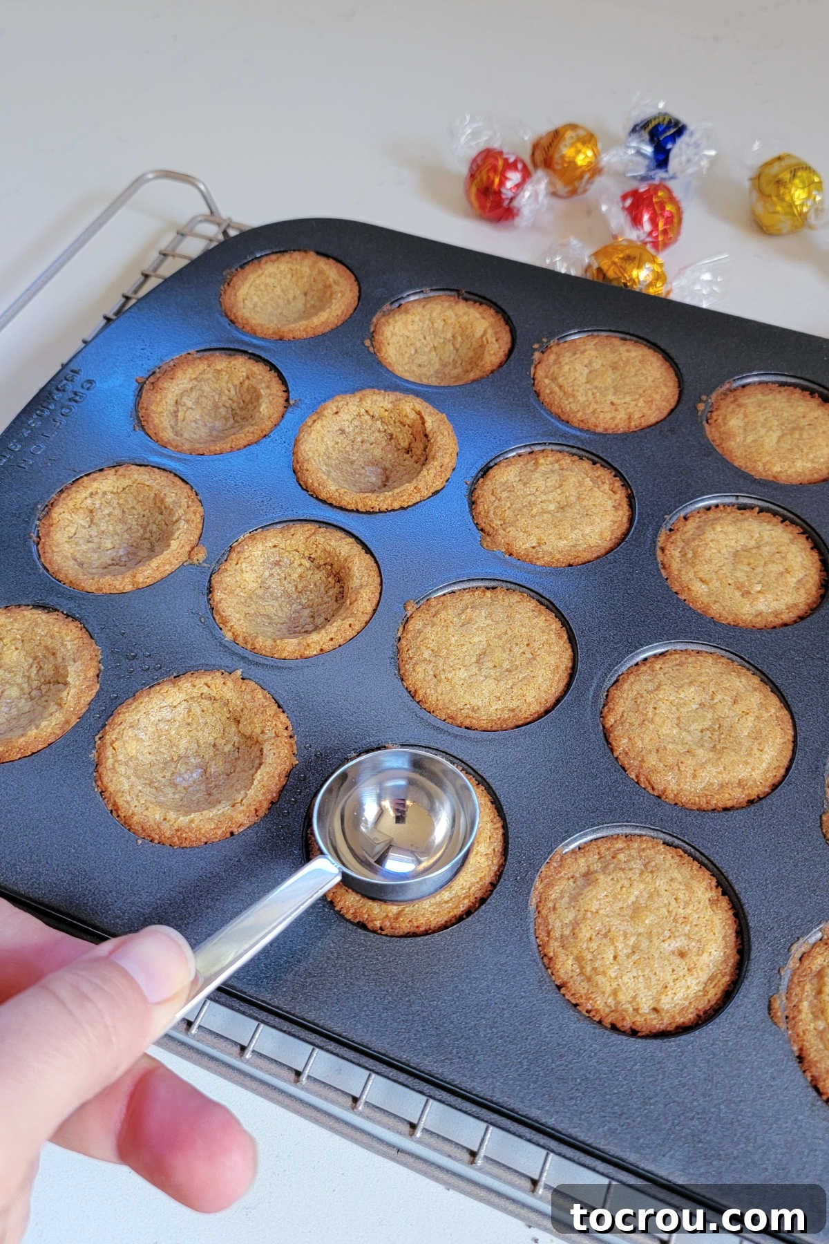 Making an indent in the freshly baked graham cookies in the mini muffin tin, making a spot for the marshmallow fluff and chocolate candy. 
