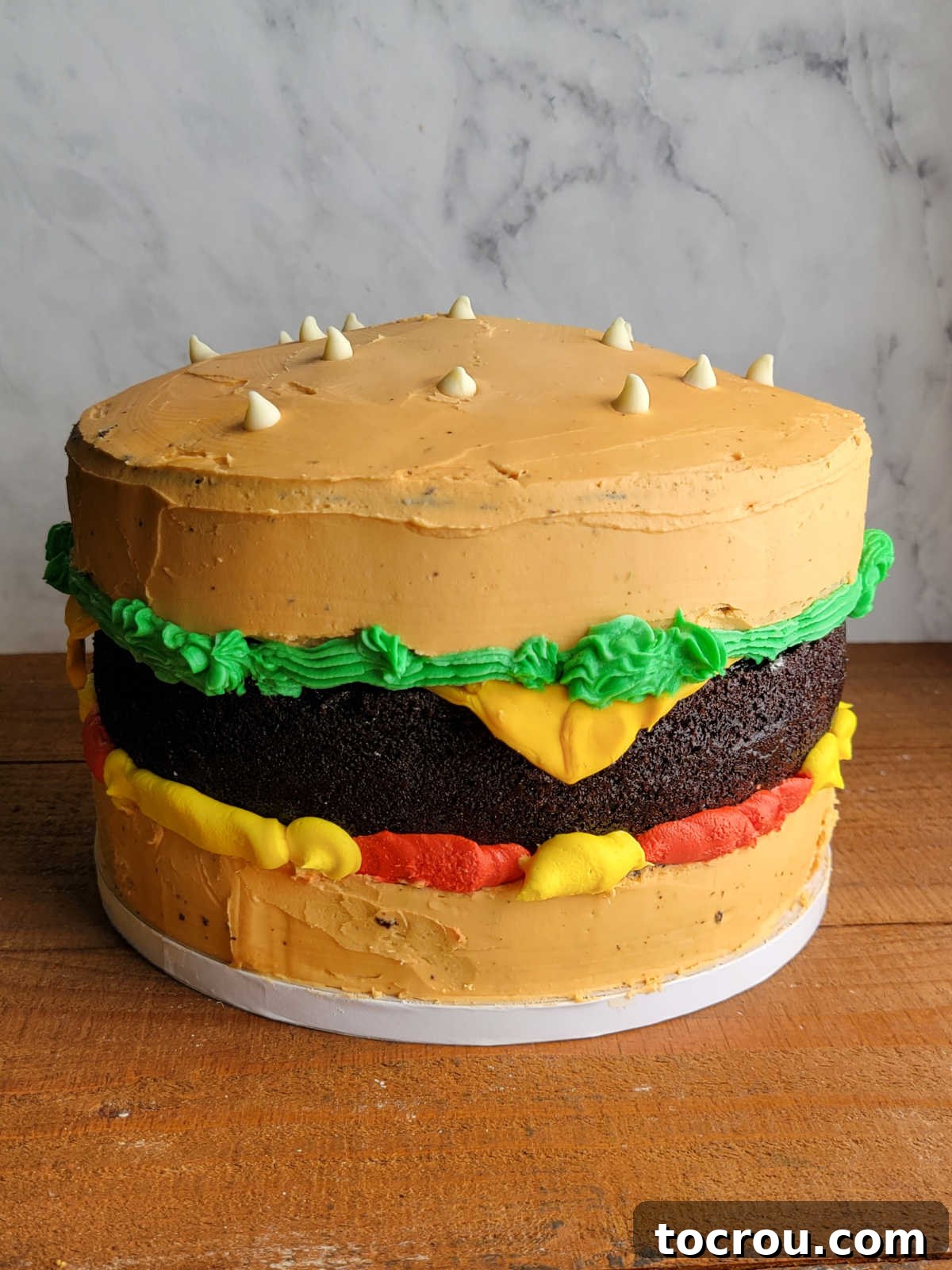 Cheeseburger Cake with Modeling Chocolate Cheese Slice Three layer chocolate cake decorated to look like a cheeseburger with lettuce, ketchup, mustard, and a modeling chocolate slice of cheese.