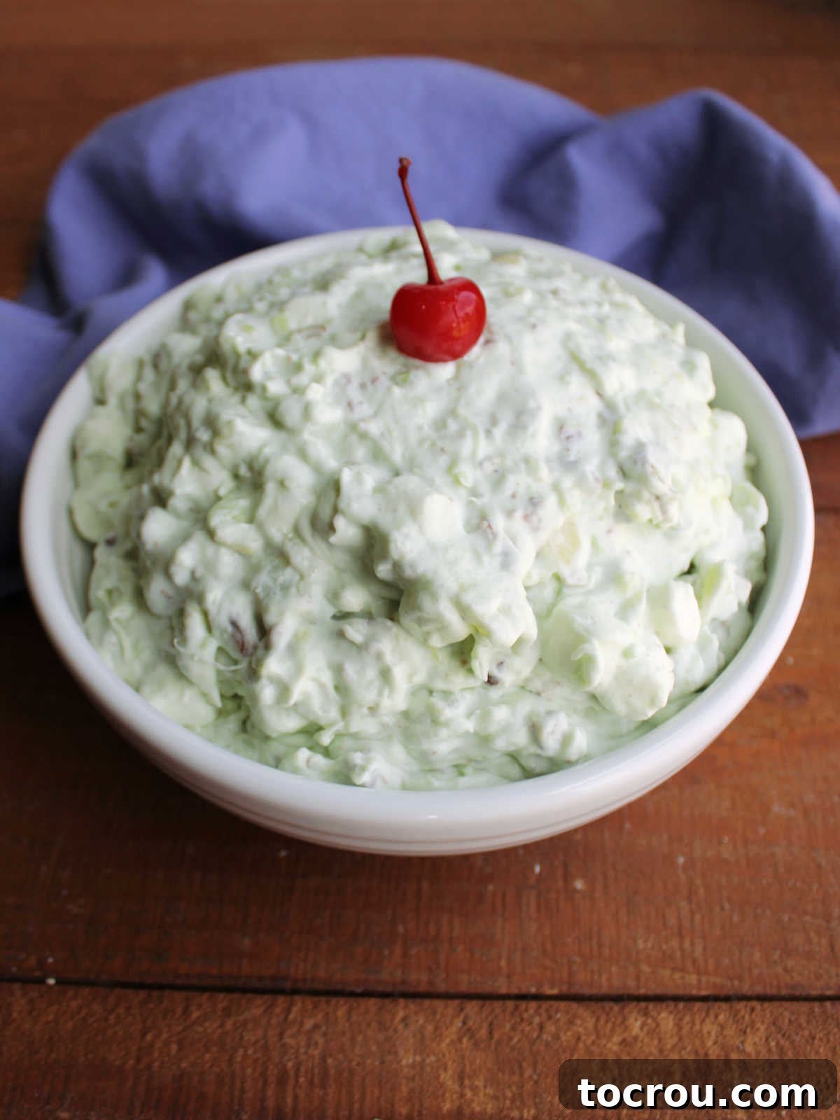 Serving bowl of cold watergate salad topped with a cherry. 