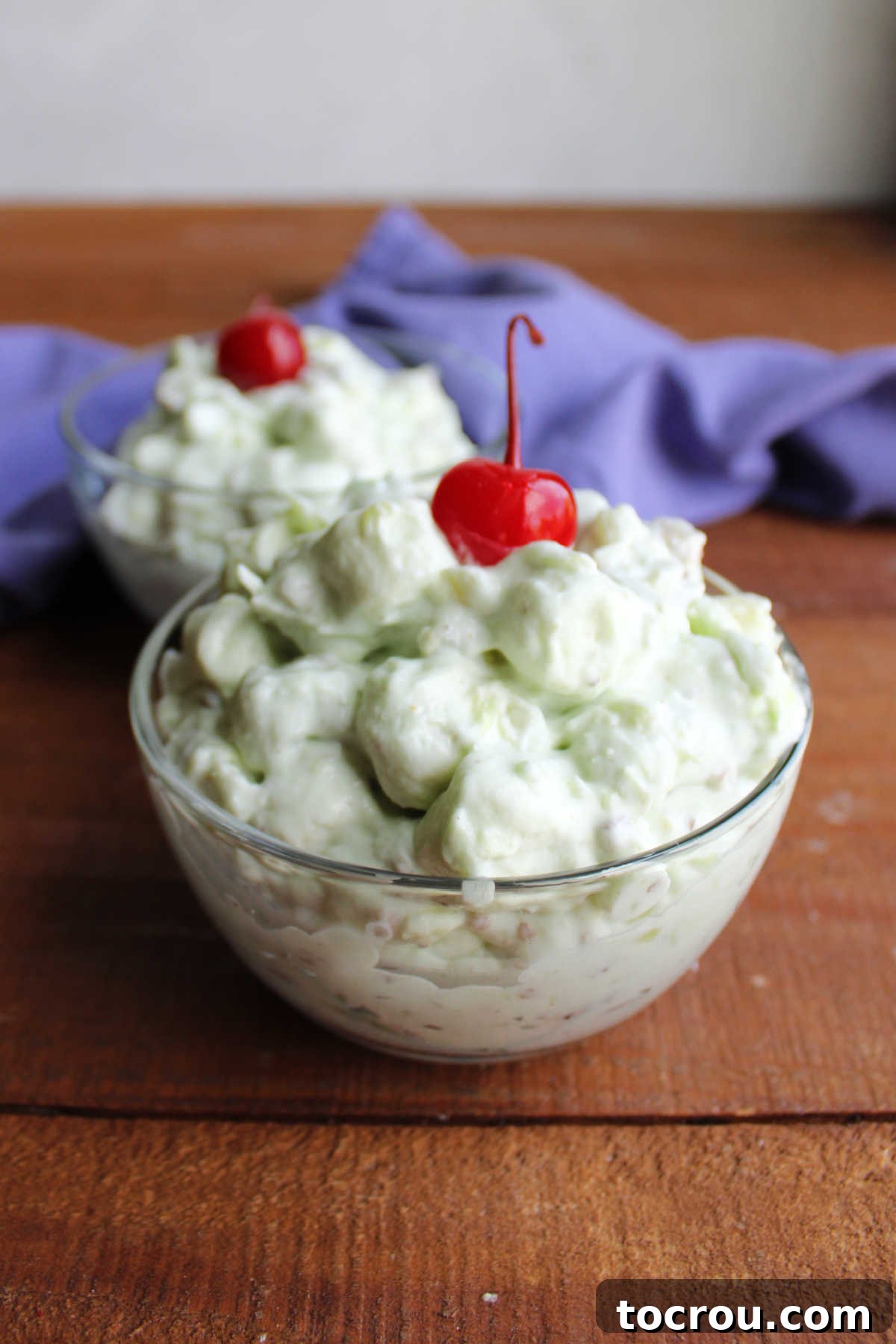 Small glass bowl of watergate salad with mini marshmallows and nuts coated in pistachio pudding and pineapple mixture. 