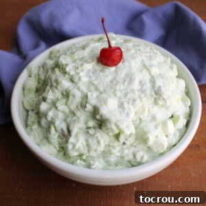 Serving bowl with pale green pistachio fluff topped with bright red maraschino cherry, ready to be served.