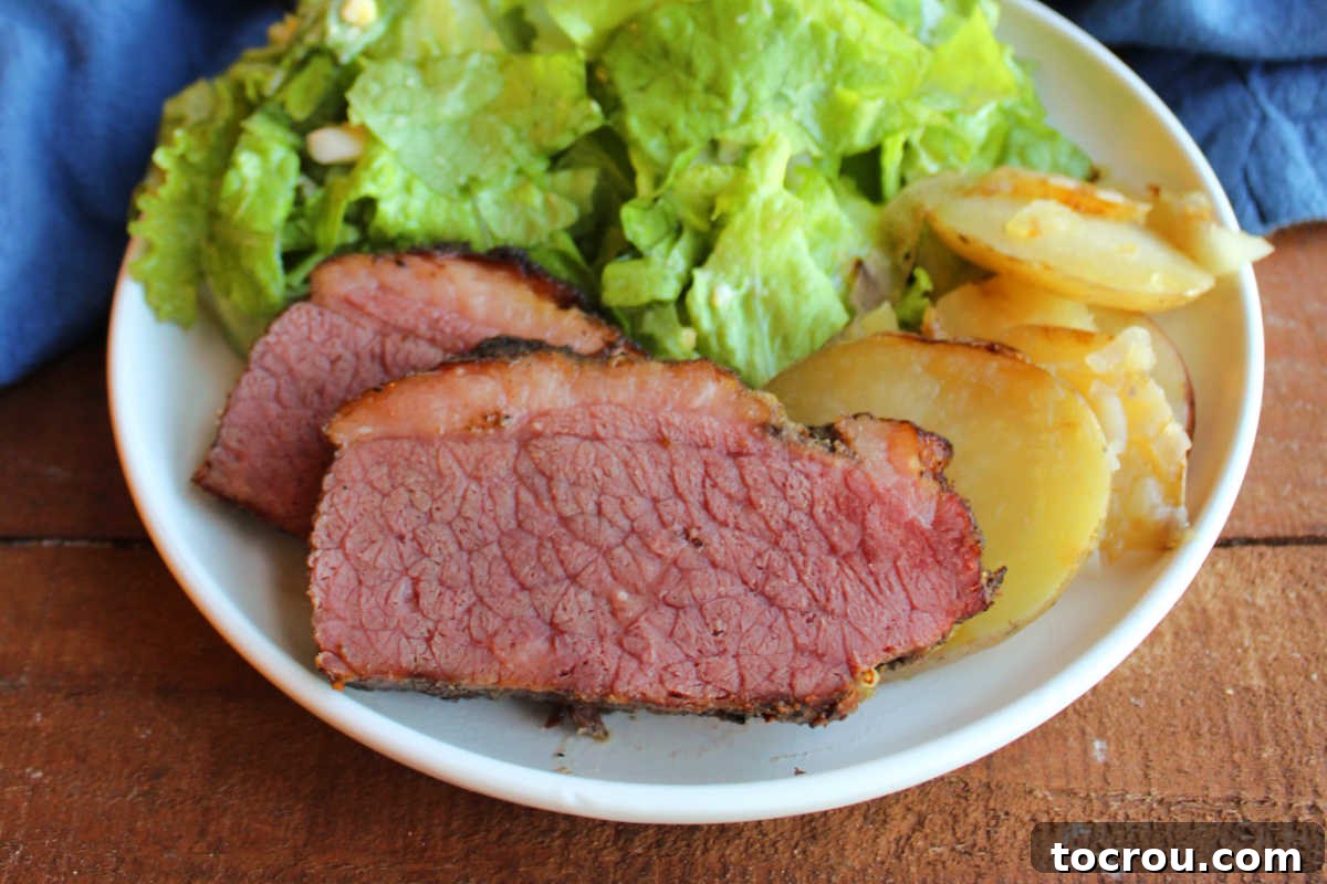 Unforgettable Pellet Smoked Corned Beef 2 Close up of perfectly sliced smoked corned beef brisket served with golden fried potatoes and a vibrant wilted lettuce salad. The meat shows a beautiful smoke ring.