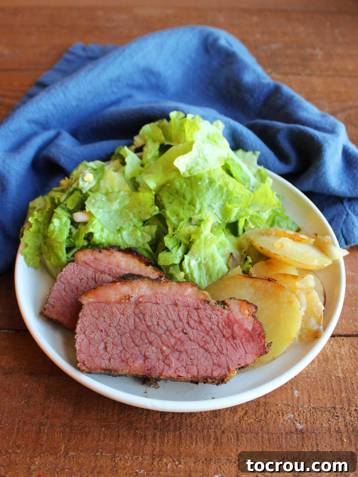 Unforgettable Pellet Smoked Corned Beef 4 A hearty dinner plate featuring generous slices of tender smoked corned beef, crispy fried potatoes, and a side of fresh wilted lettuce salad.
