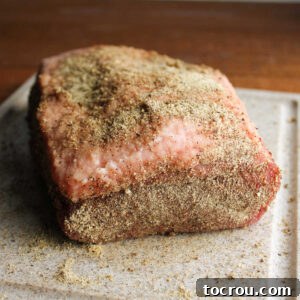 Raw corned beef flat covered in a black pepper heavy seasoning mix, ready to go on the smoker.