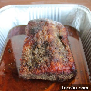 Smoked corned beef brisket in pan with water and seasonings, covered with foil.