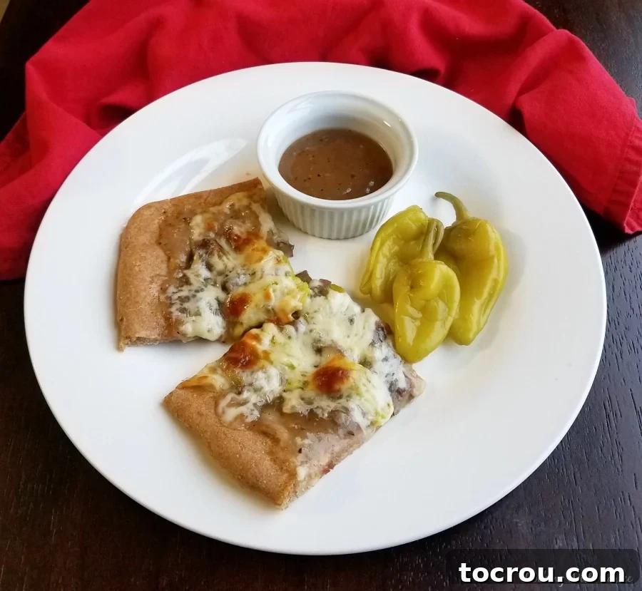 Two pieces of Italian beef pizza served with pepperoncini and a ramekin of gravy.