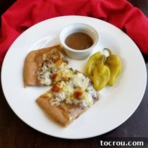Two pieces of Italian beef pizza served with pepperoncini and a ramekin of gravy.