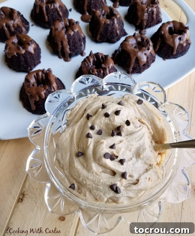 A large glass bowl filled with creamy peanut butter whipped cream and mini chocolate chips, with a platter of mini bundt cakes blurred in the background.