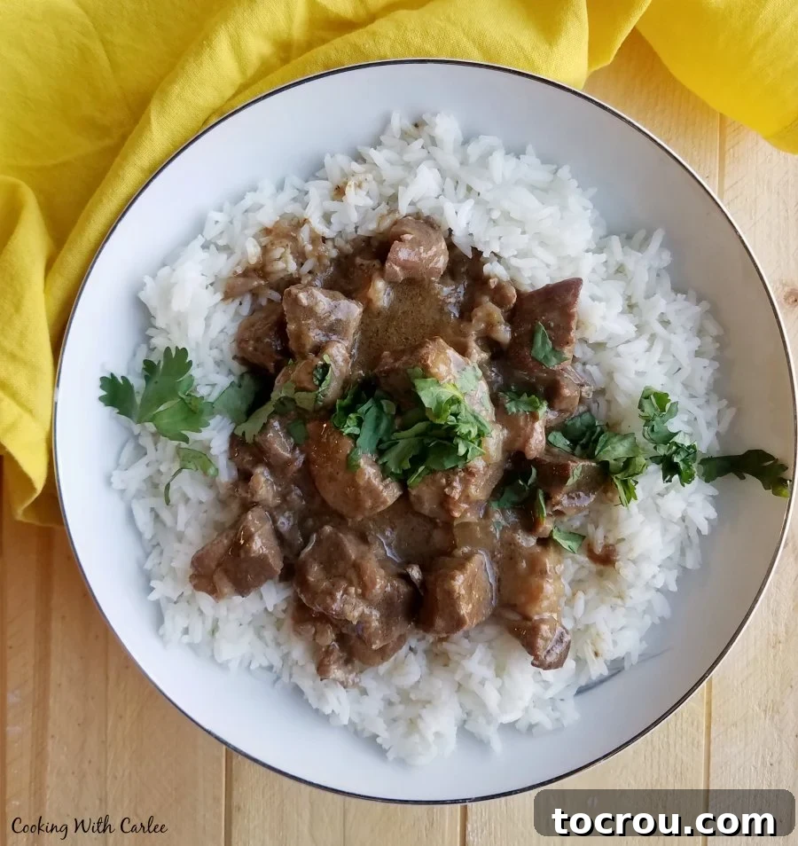 A steaming bowl of Maw-Maw's flavorful lamb curry stew, served over fluffy white rice and garnished with fresh herbs, ready to be enjoyed.