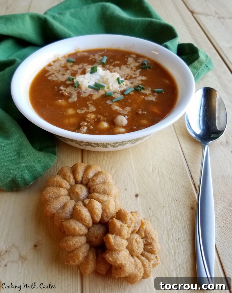 These chili cheese spritz crackers perfectly complement a warm bowl of chili. Bowl of chili topped with sour cream and cheese next to homemade flower shaped cheese crackers.